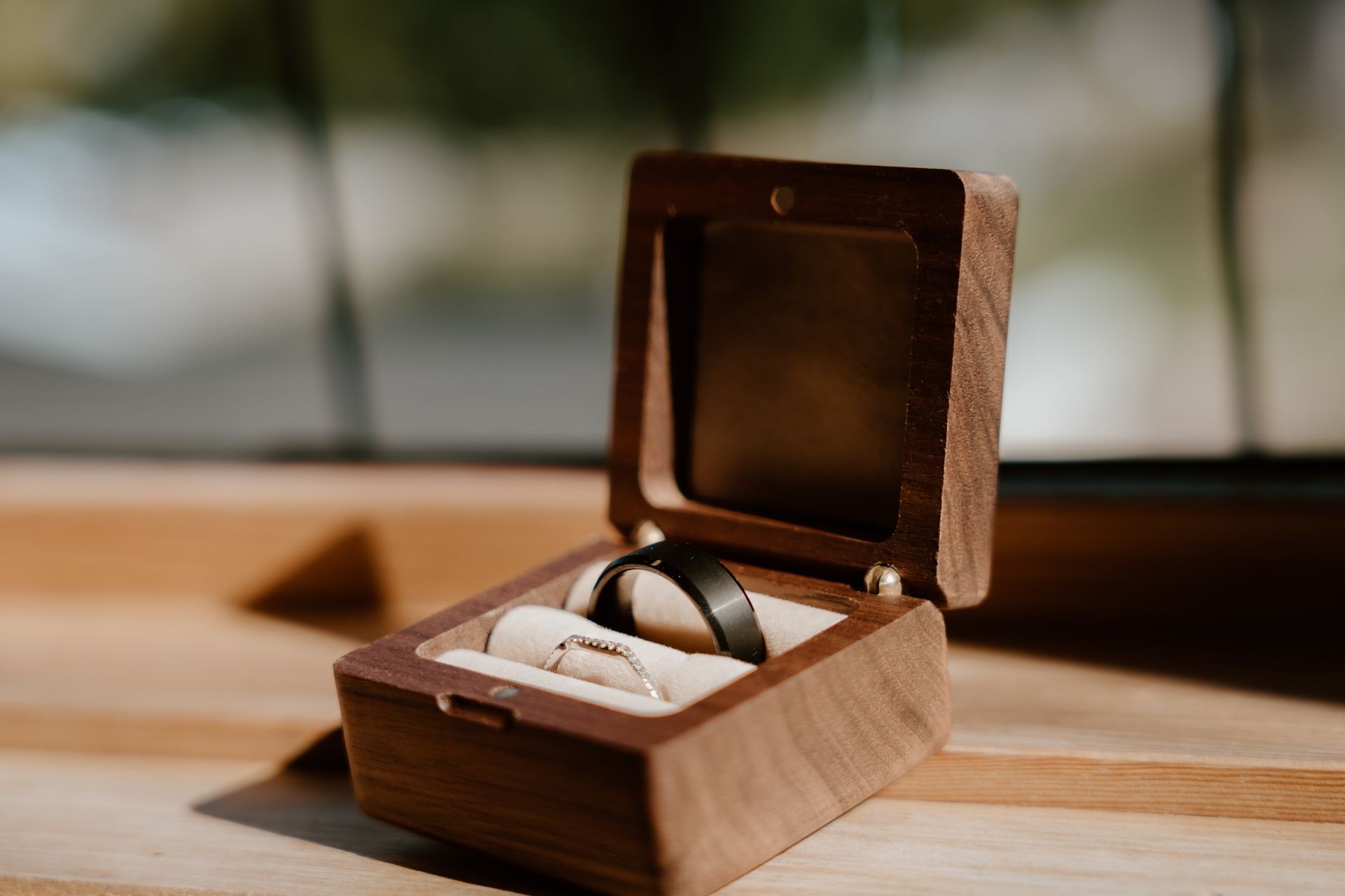 Two wedding rings are in a wooden box on a table.
