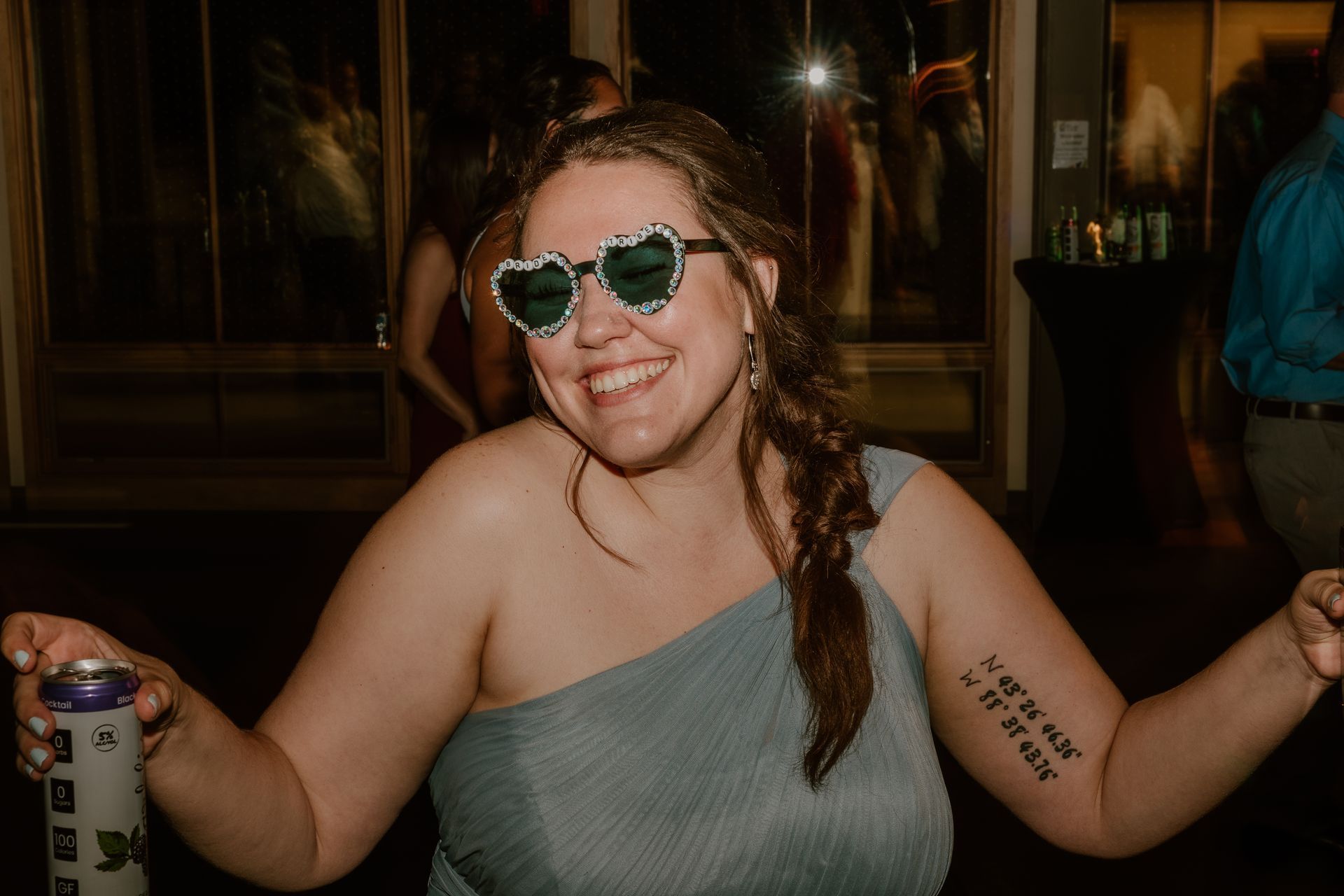 A woman wearing sunglasses is holding a can of beer and smiling.