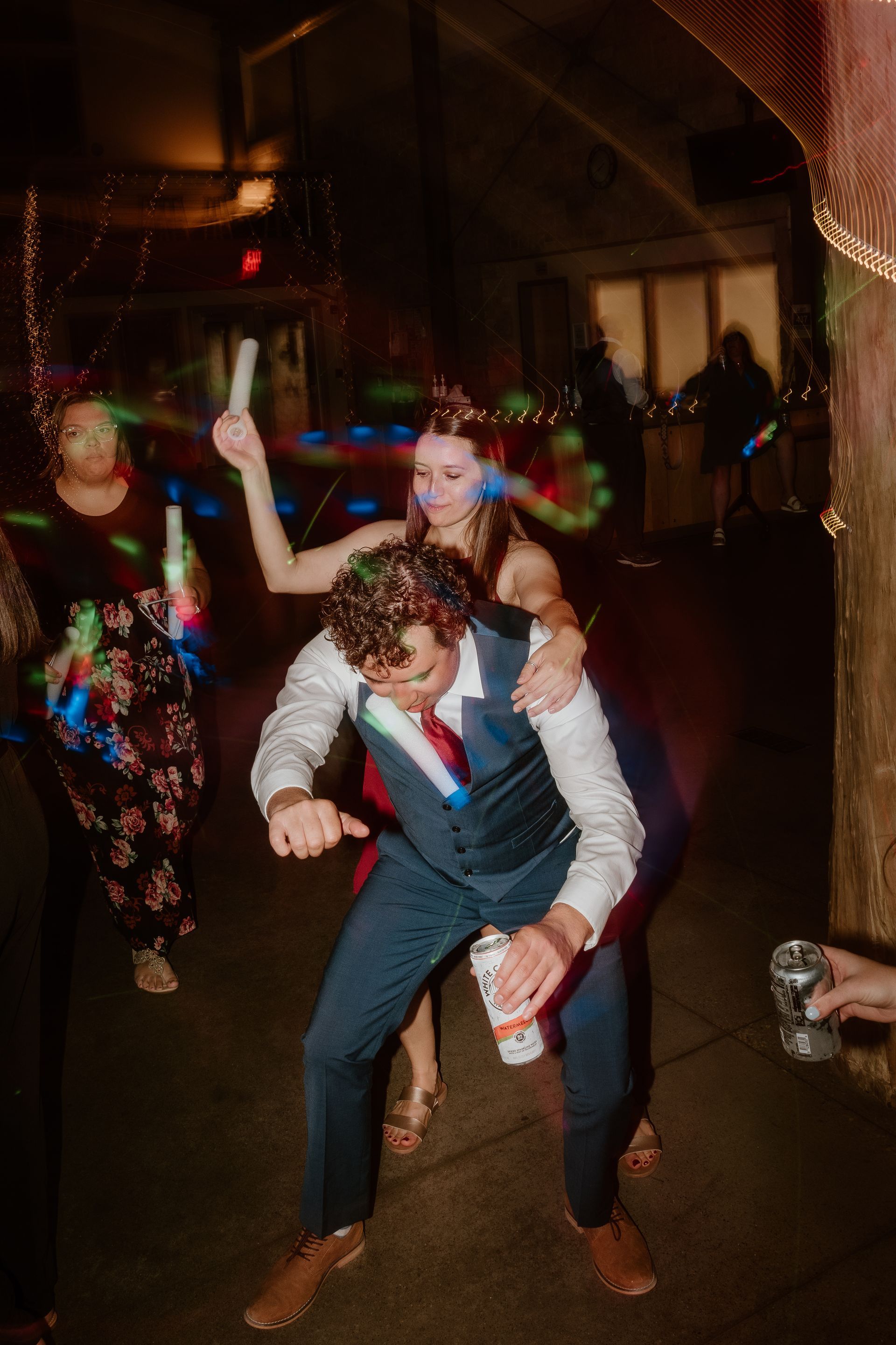 A man is carrying a woman on his shoulders at a wedding reception.