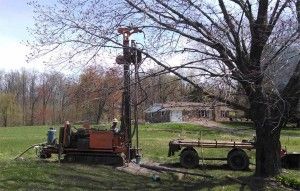 A drill is sitting on top of a trailer in a field next to a tree.