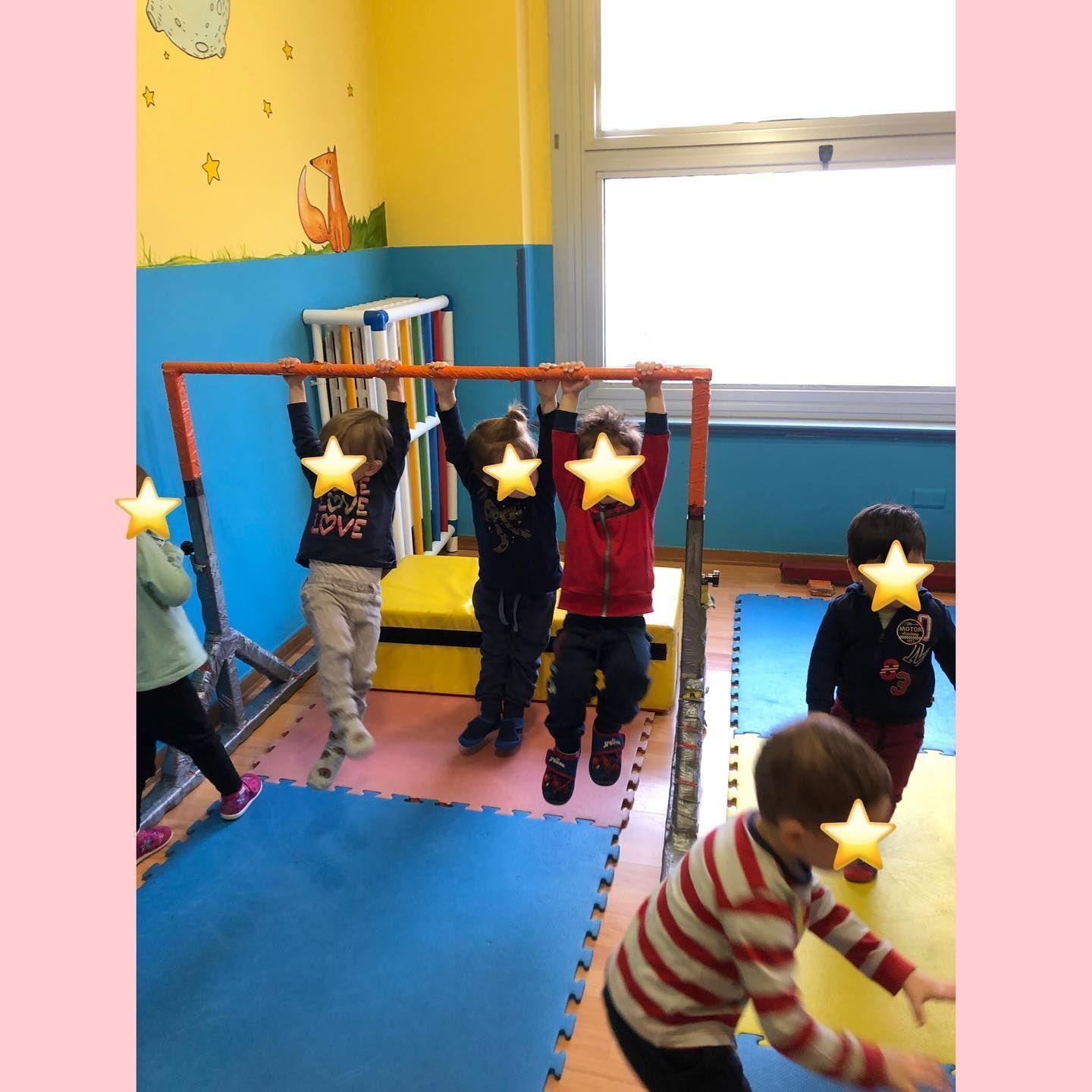Bambini che giocano su una sbarra in un'aula dai colori vivaci. Alcuni si appendono, altri guardano.