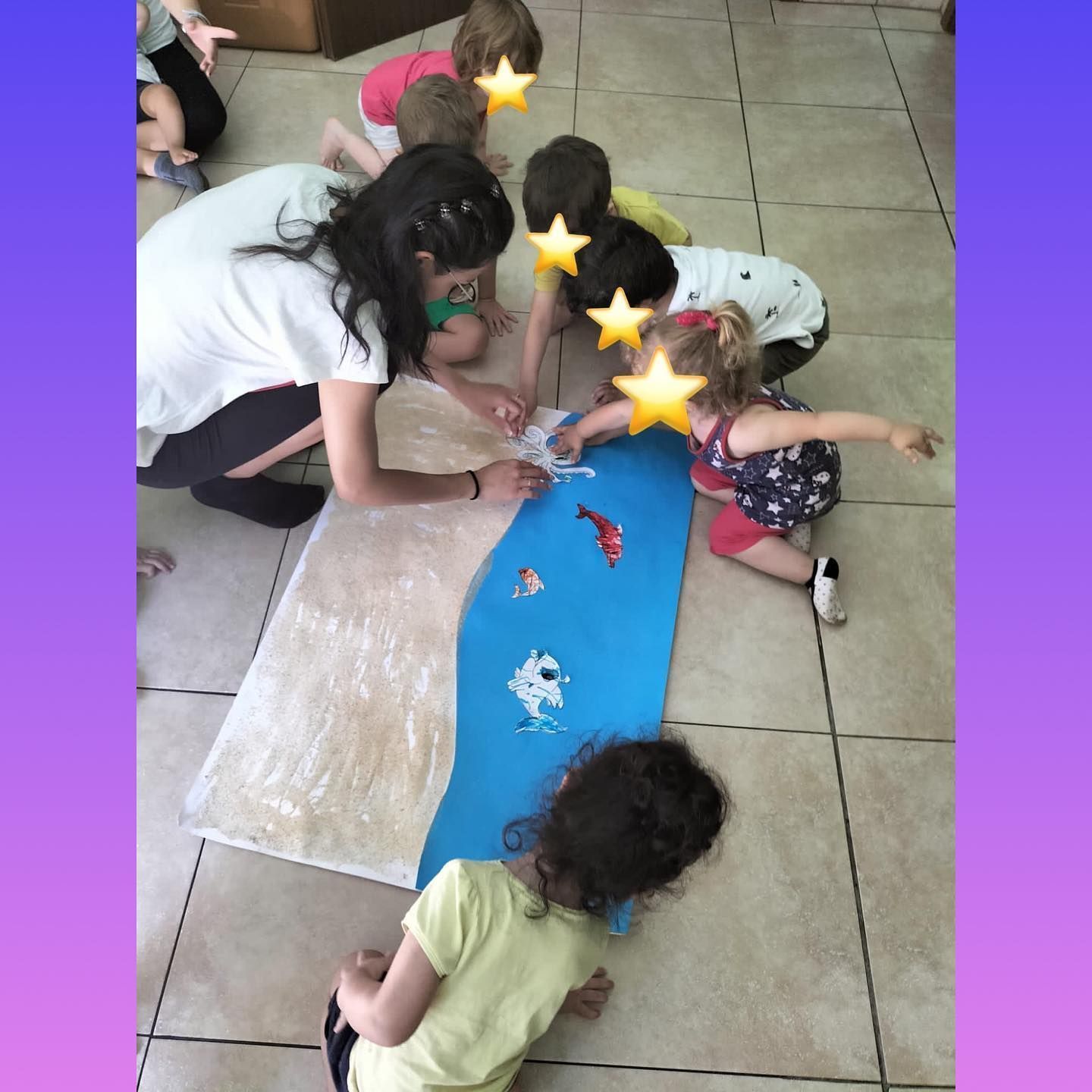 I bambini e un insegnante si riuniscono attorno a un progetto artistico raffigurante un fiume azzurro sul pavimento, decorandolo con dei pesci.