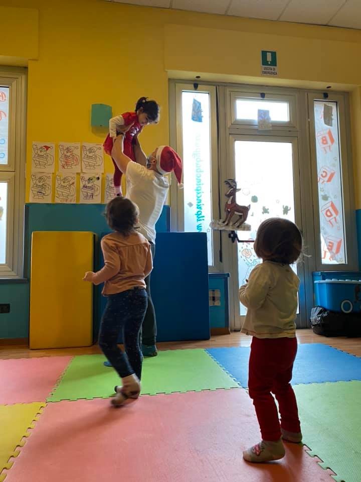 Una persona con un cappello da Babbo Natale solleva un bambino mentre altri bambini lo guardano in una sala giochi colorata.