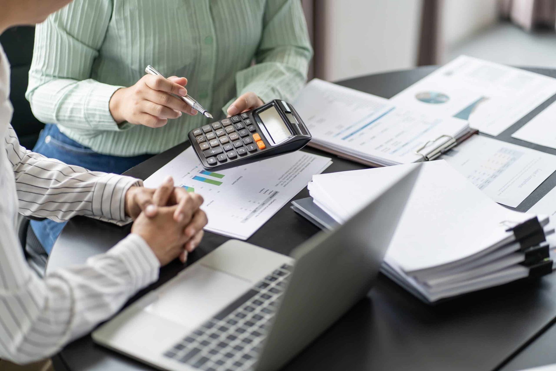 A Man and A Woman Are Sitting at A Table with A Laptop and A Calculator — Blue Orchid Accounting In Woongarrah, NSW