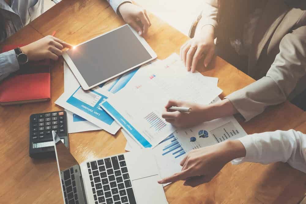 A Group of People Are Sitting at A Table Looking at Papers and A Laptop — Blue Orchid Accounting In Woongarrah, NSW