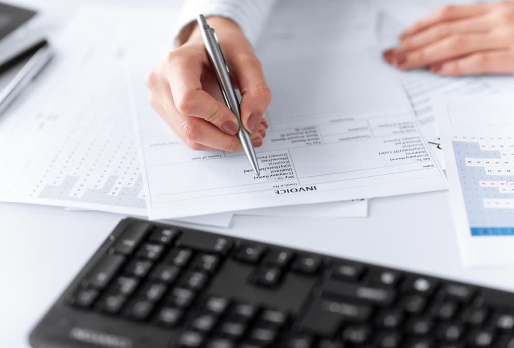 A Person Is Writing on A Piece of Paper Next to A Keyboard — Blue Orchid Accounting In Woongarrah, NSW