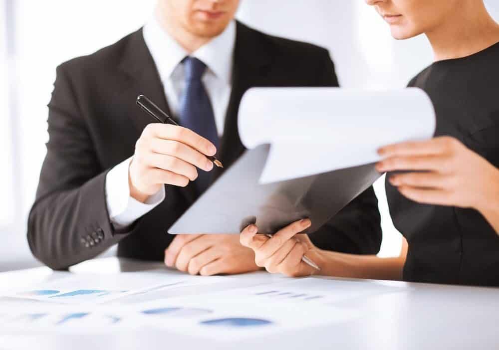 A Man and A Woman Are Sitting at A Table Looking at A Piece of Paper — Blue Orchid Accounting In Woongarrah, NSW