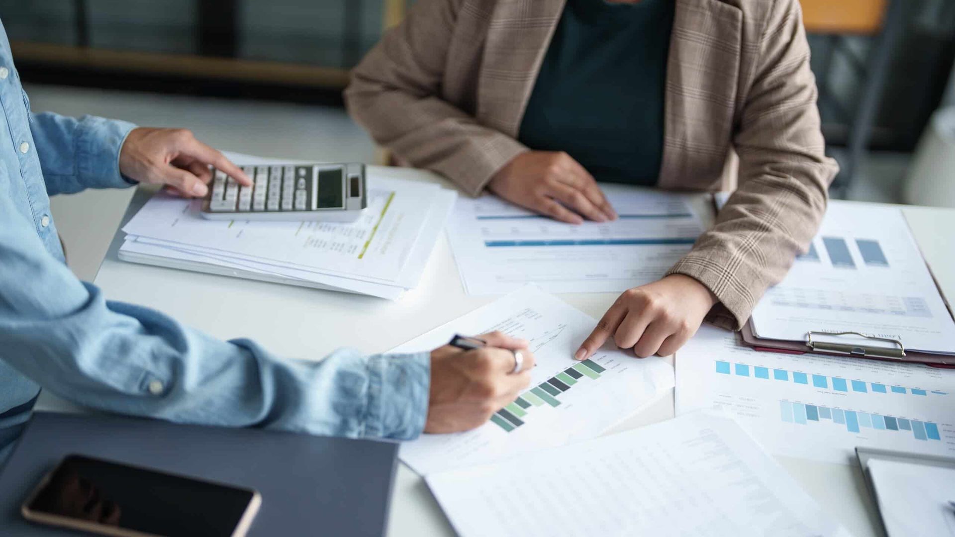 Two People Are Sitting at A Table with Papers and A Calculator — Blue Orchid Accounting In Woongarrah, NSW