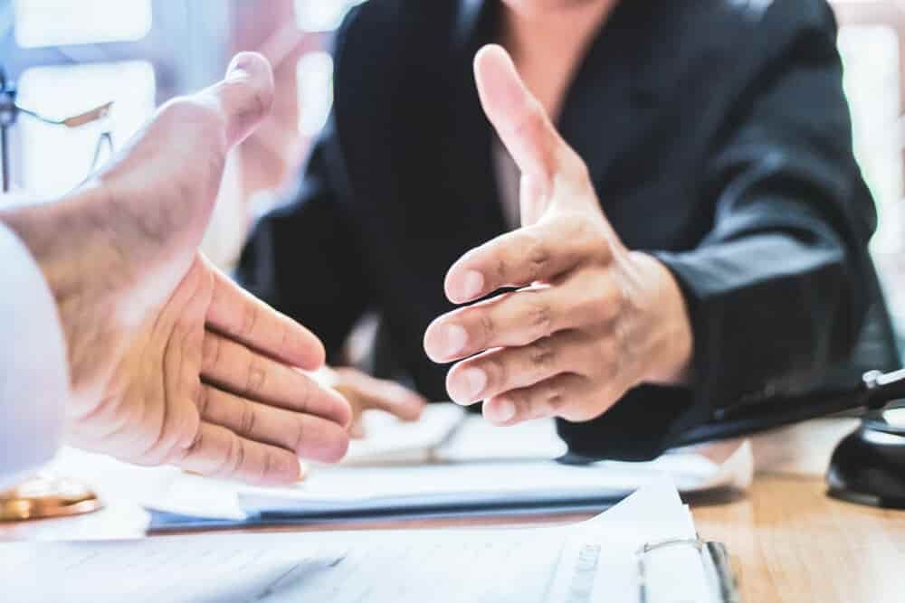 A Man and A Woman Are Shaking Hands Over a Table — Blue Orchid Accounting In Woongarrah, NSW
