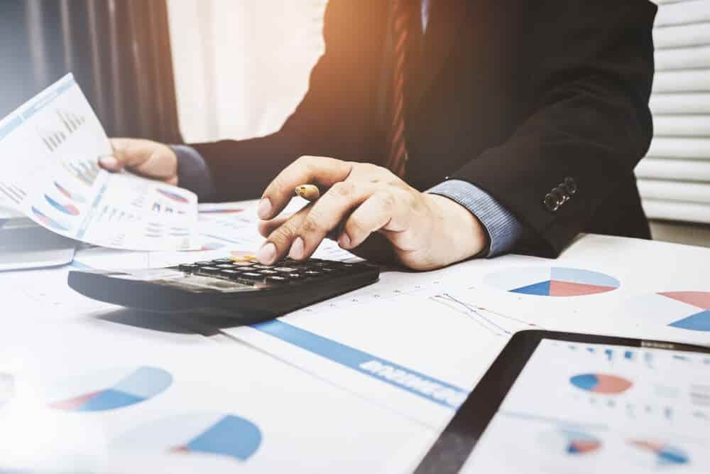 A Man Is Sitting at A Desk Using a Calculator and A Pen — Blue Orchid Accounting In Woongarrah, NSW