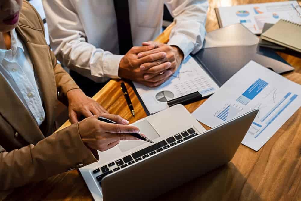 A Man and A Woman Are Sitting at A Table Looking at A Laptop Computer — Blue Orchid Accounting In Woongarrah, NSW