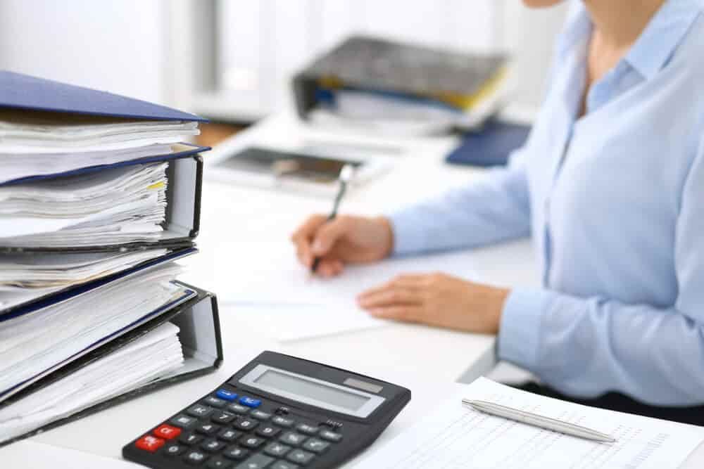 A Woman Is Sitting at A Desk with A Calculator and A Pen — Blue Orchid Accounting In Woongarrah, NSW