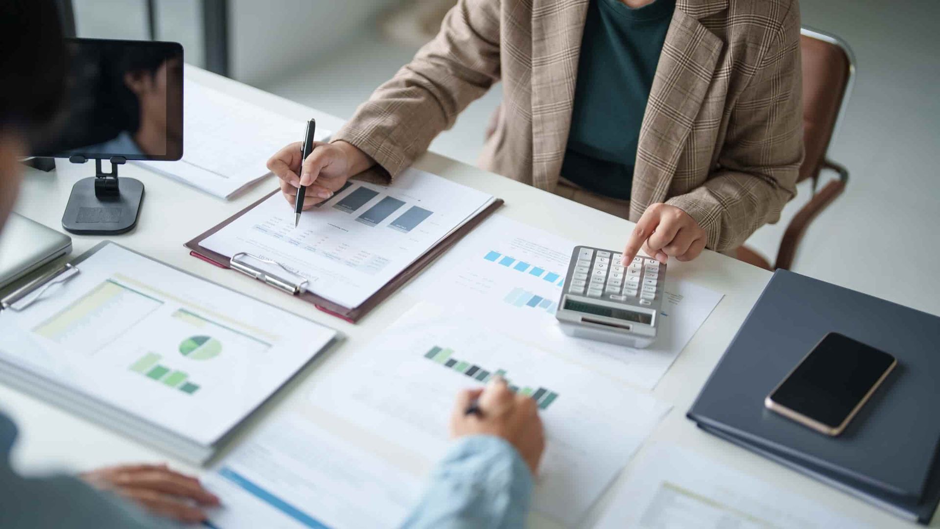 A Woman Is Sitting at A Table Using a Calculator — Blue Orchid Accounting In Woongarrah, NSW