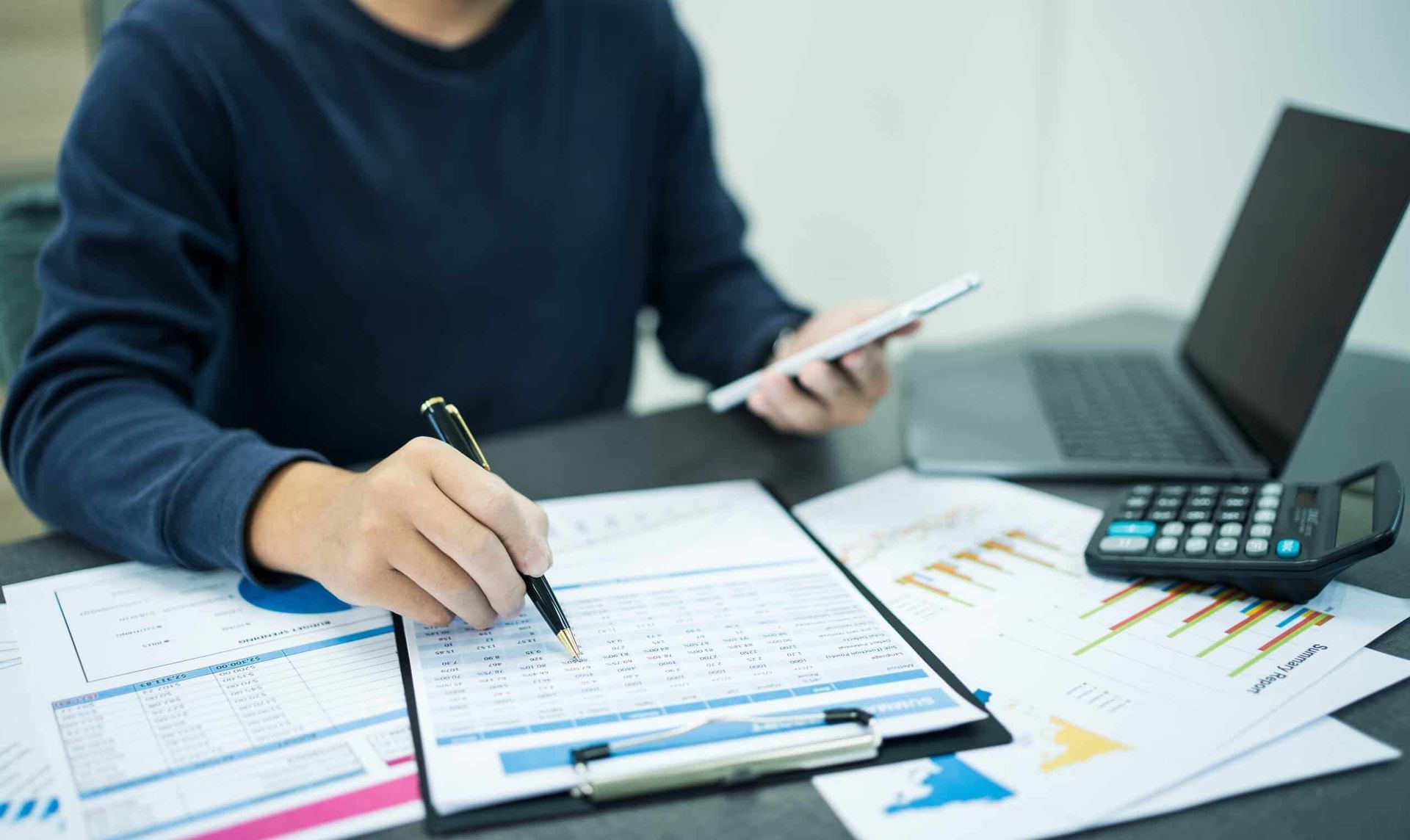 A Man Is Sitting at A Desk Using a Tablet and A Calculator — Blue Orchid Accounting In Woongarrah, NSW