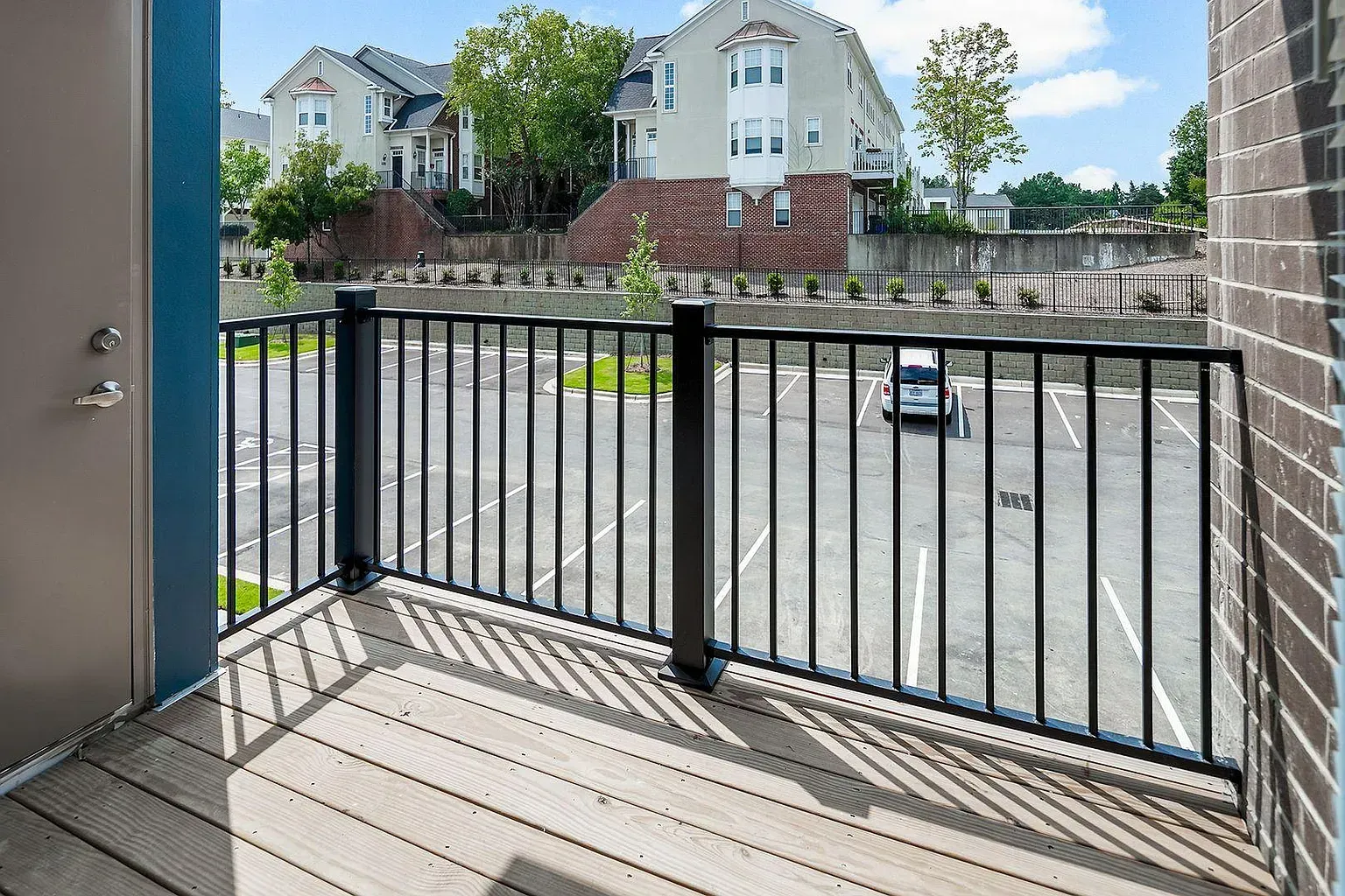 Balcony overlooking a parking lot. Black railing, wood deck, building exterior.