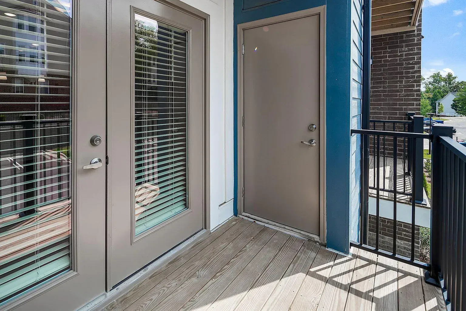 Balcony with gray doors, a storage door, and a black railing. Brown wood-look floor. Blue wall.