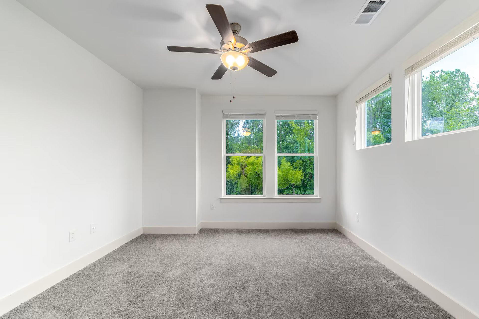 Empty bedroom with gray carpet, white walls, windows, and a ceiling fan.