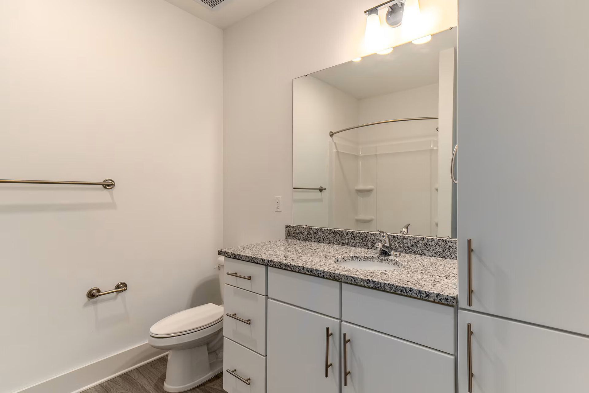Modern bathroom with white cabinets, granite countertop, toilet, and large mirror.