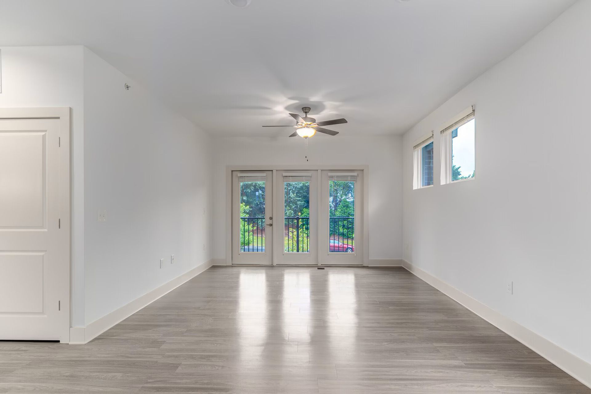 Empty, bright living room with white walls, gray floors, and doors to a balcony.