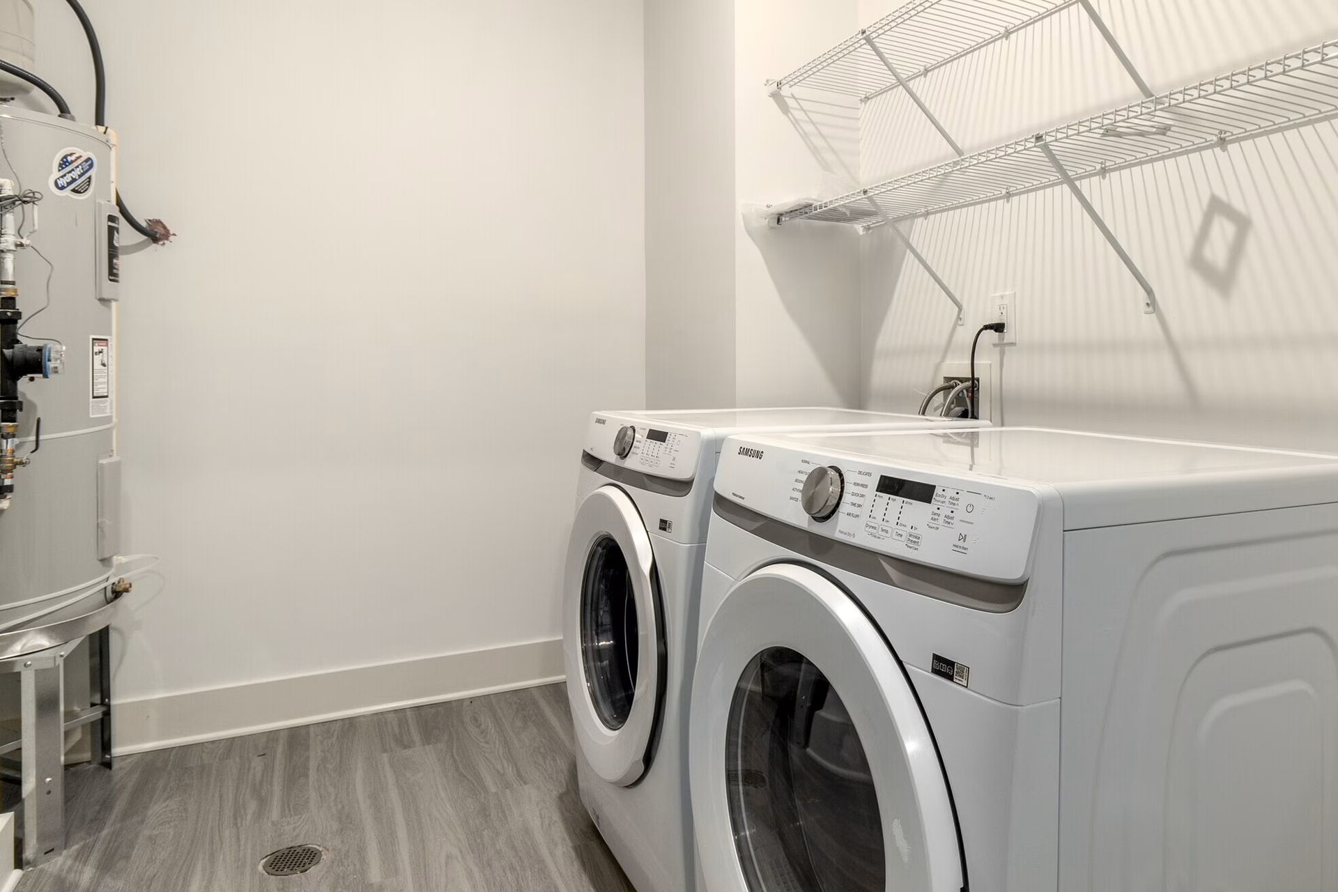 Laundry room with a washer, dryer, and shelving unit. Grey flooring, white walls.