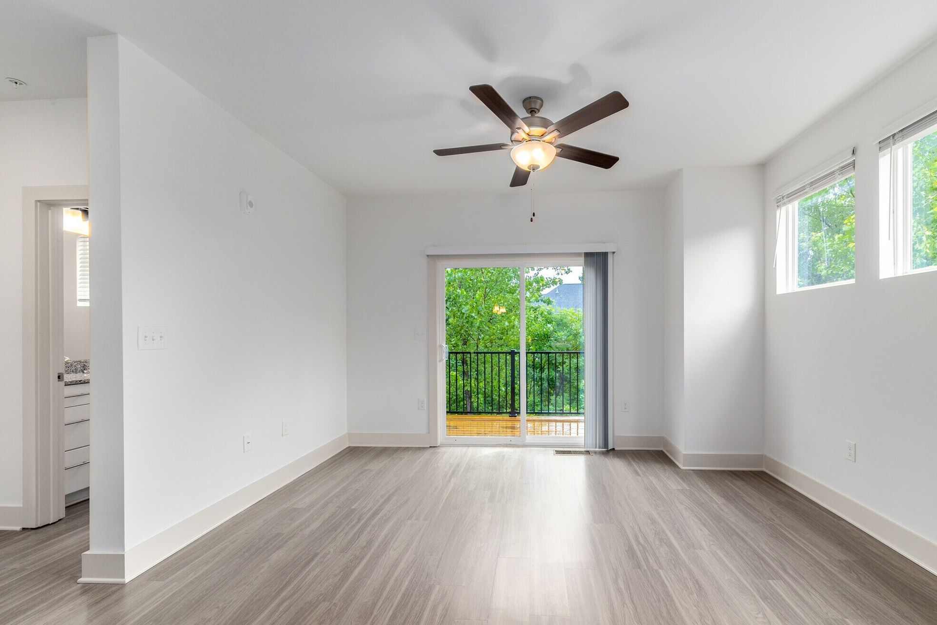 Empty room with wood-look floor, white walls, a ceiling fan, and a sliding door leading to a balcony.