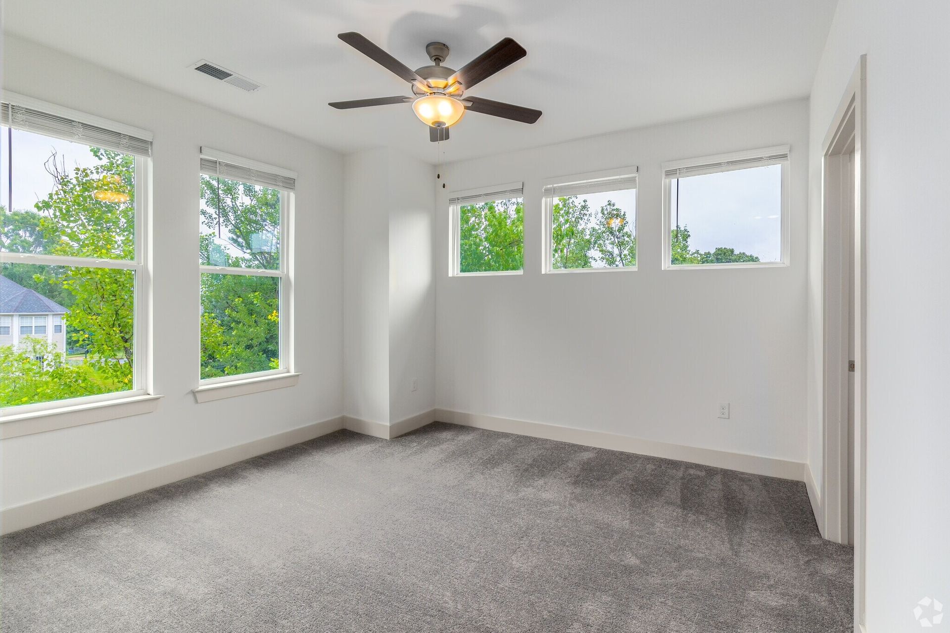 Empty bedroom with gray carpet, white walls, windows, and a ceiling fan.