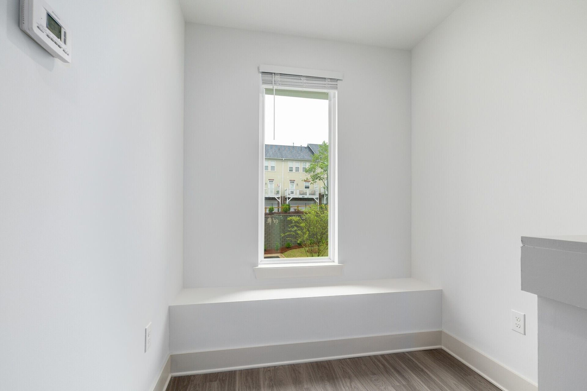 Interior room with narrow window, white walls, window seat, and wood-look flooring.