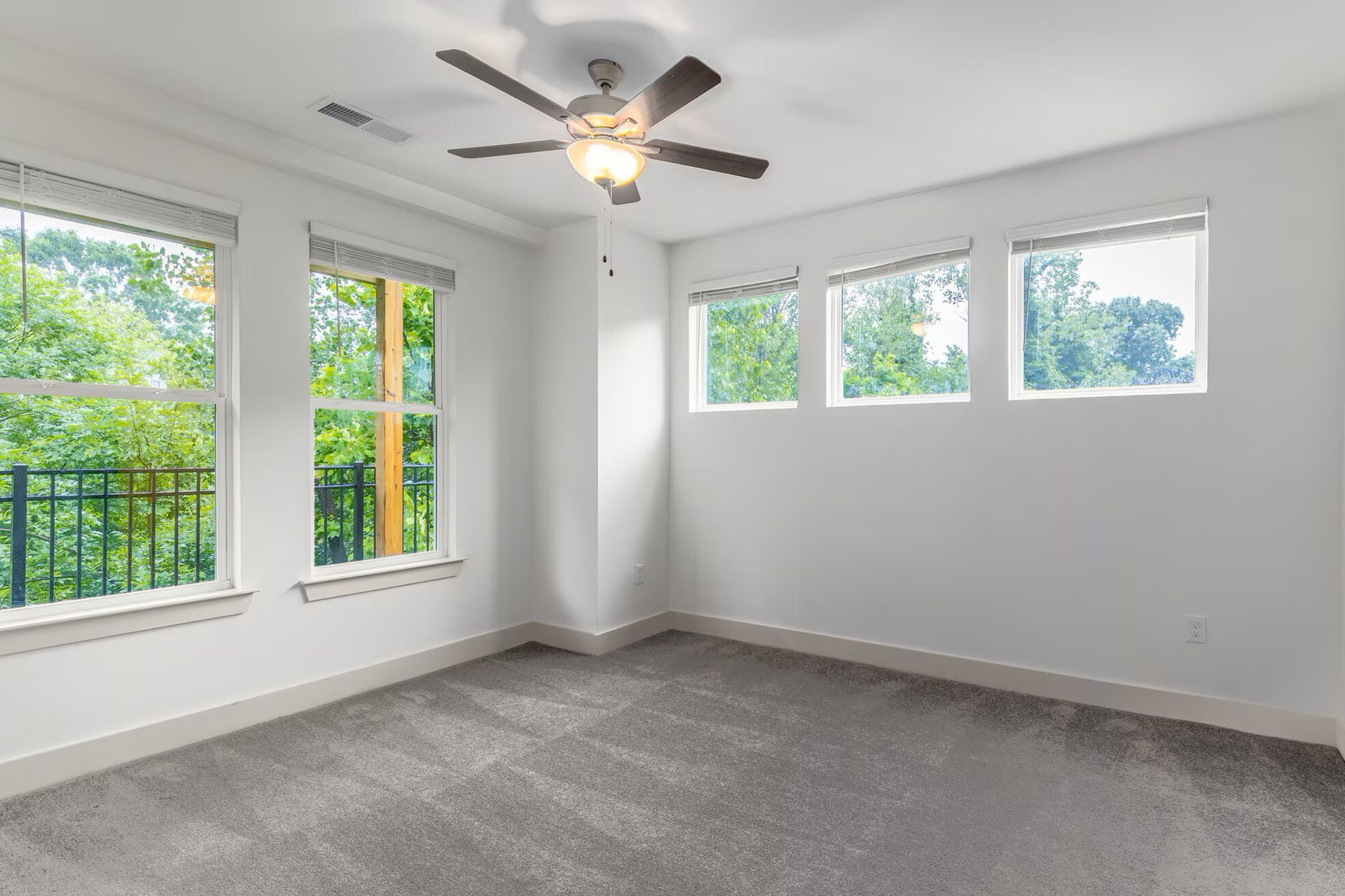 Empty bedroom with gray carpet, white walls, windows, and a ceiling fan.