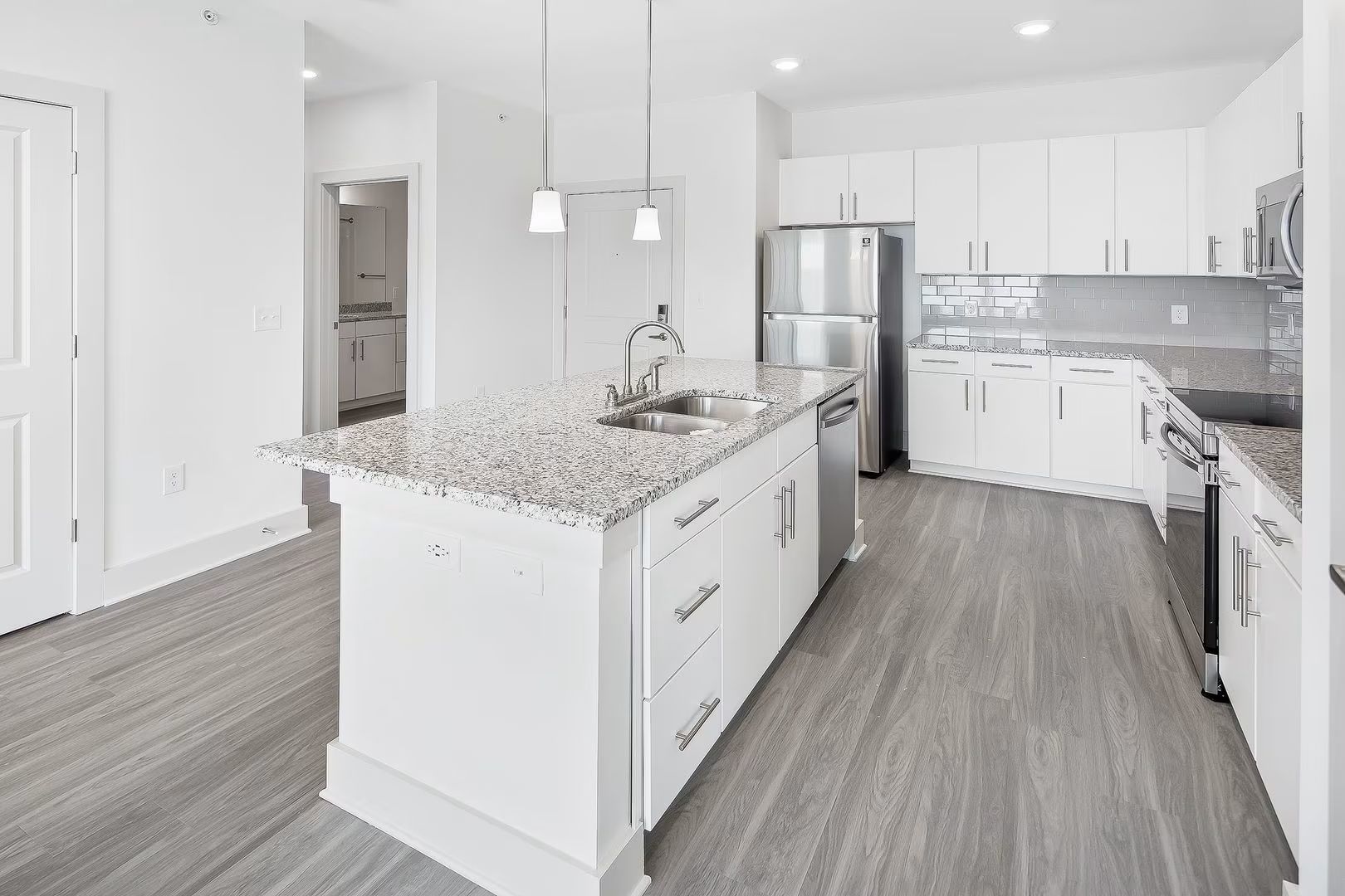Modern white kitchen with island, granite countertops, stainless steel appliances, and gray flooring.