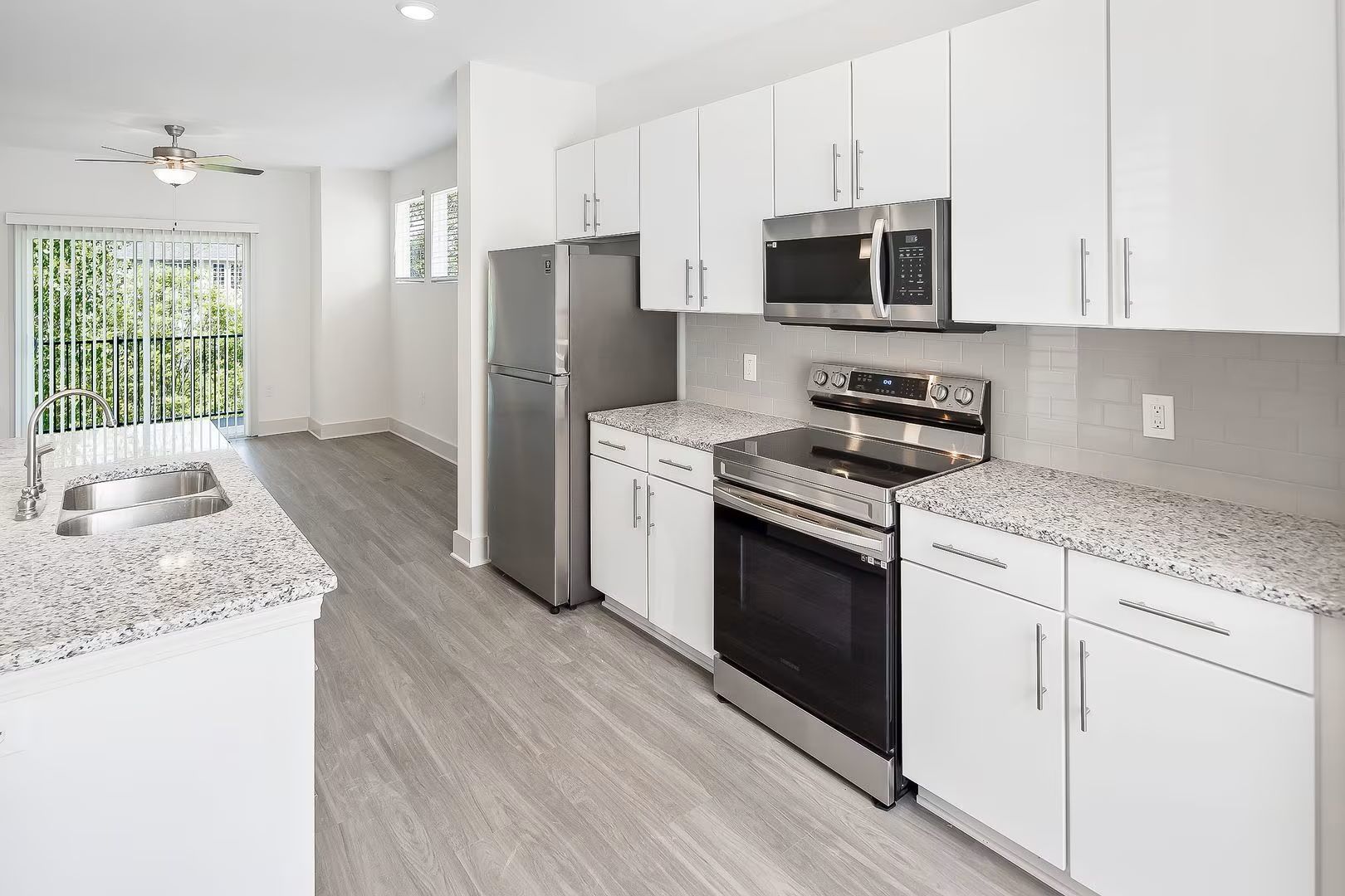 Modern kitchen with white cabinets, granite countertops, stainless steel appliances, and gray flooring.