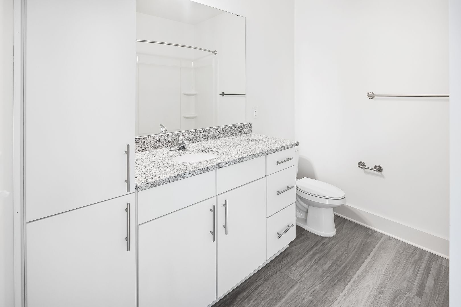 White bathroom with gray countertop, sink, and toilet, dark wood-look flooring.