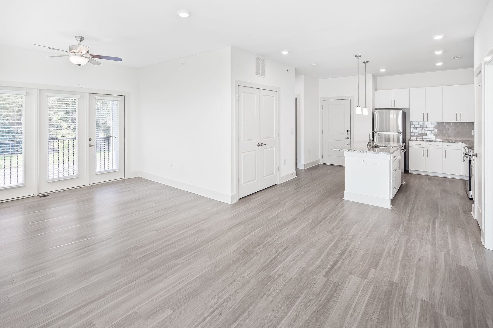 Empty, modern apartment interior with gray flooring, white walls, and a kitchen.