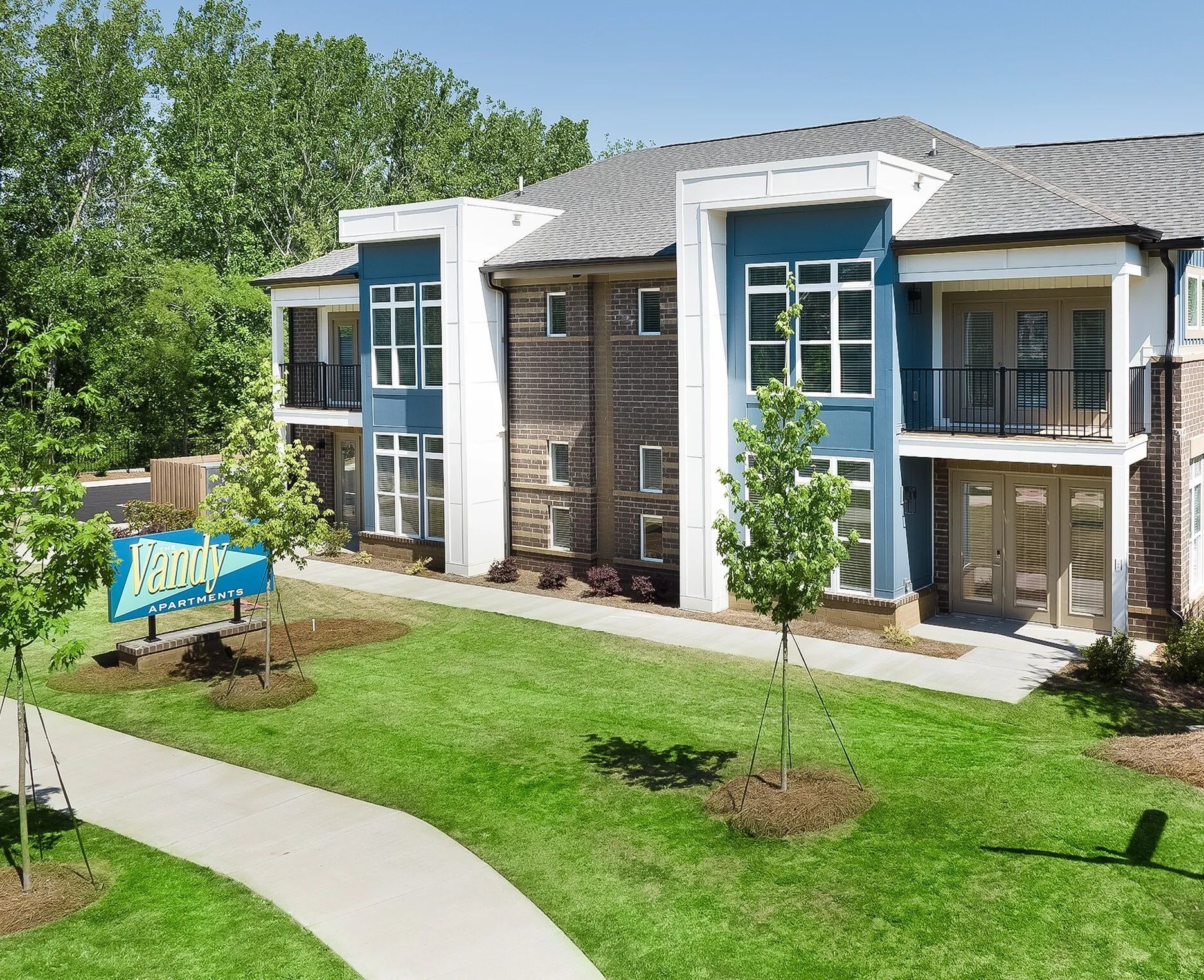 Apartment complex with teal accents, brick facade, and a grassy lawn with a sidewalk.