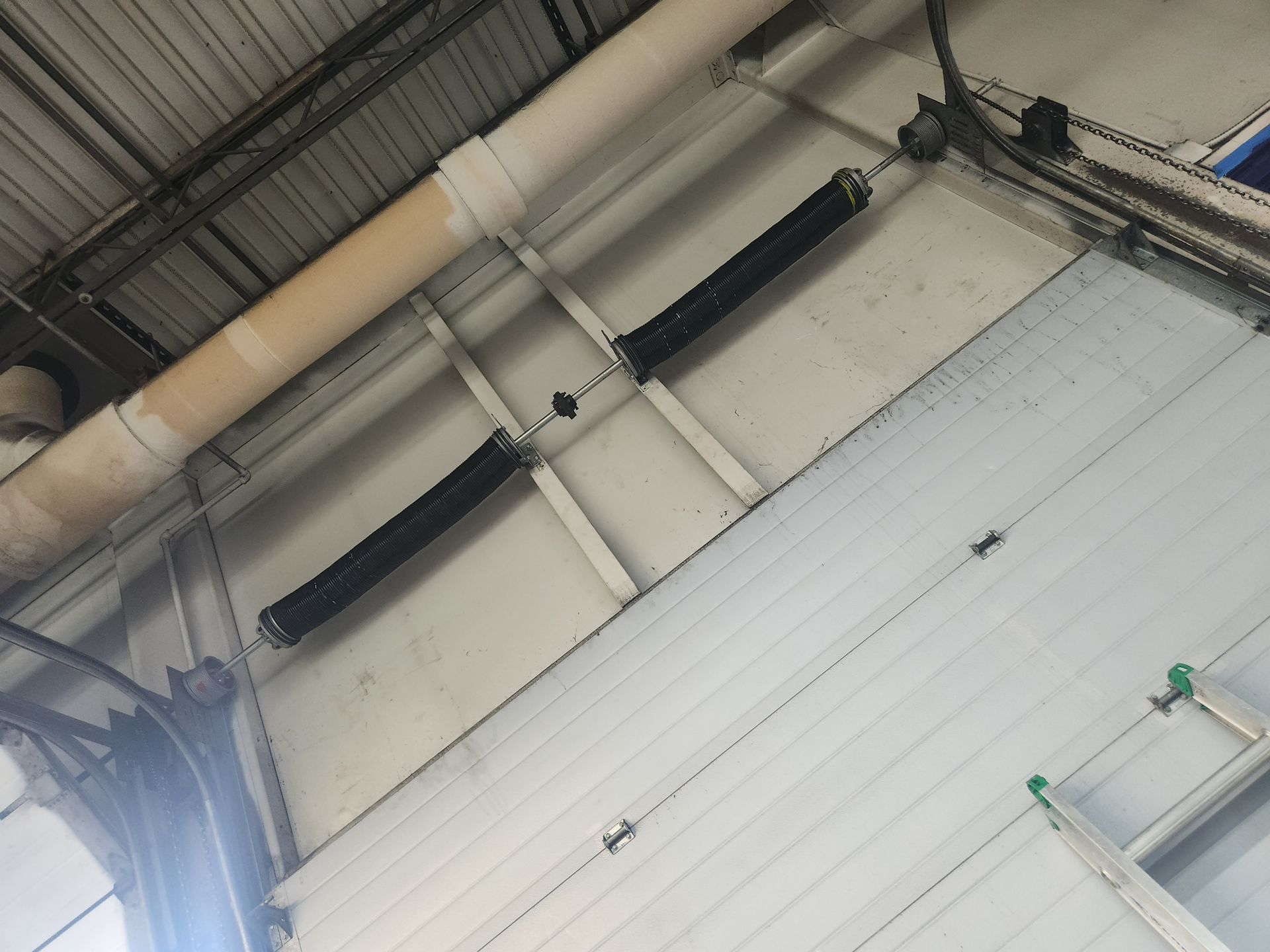 Garage door springs attached to the ceiling above a white door.