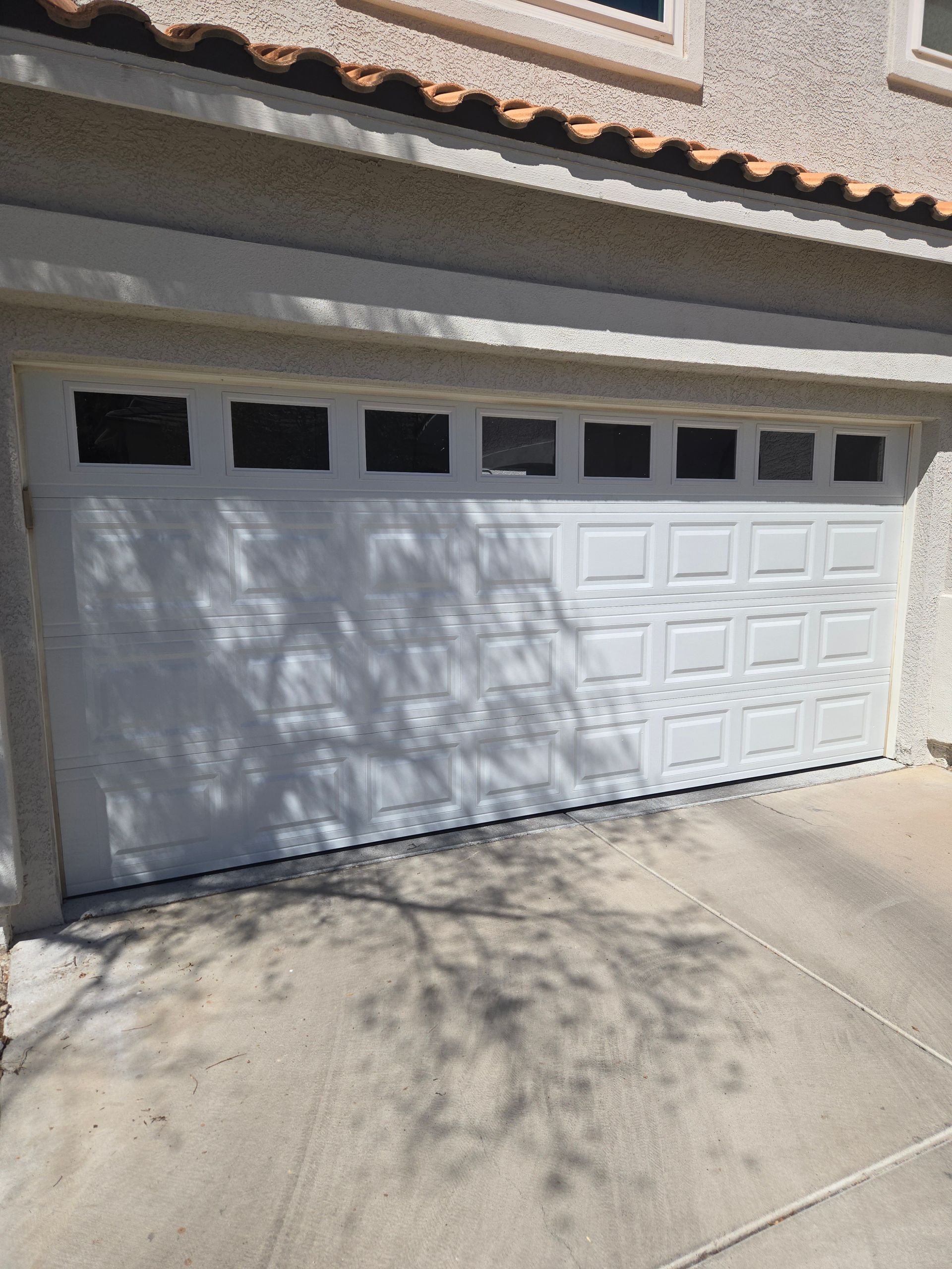 White garage door with windows above, set in a stucco building, visible shadow on concrete driveway.