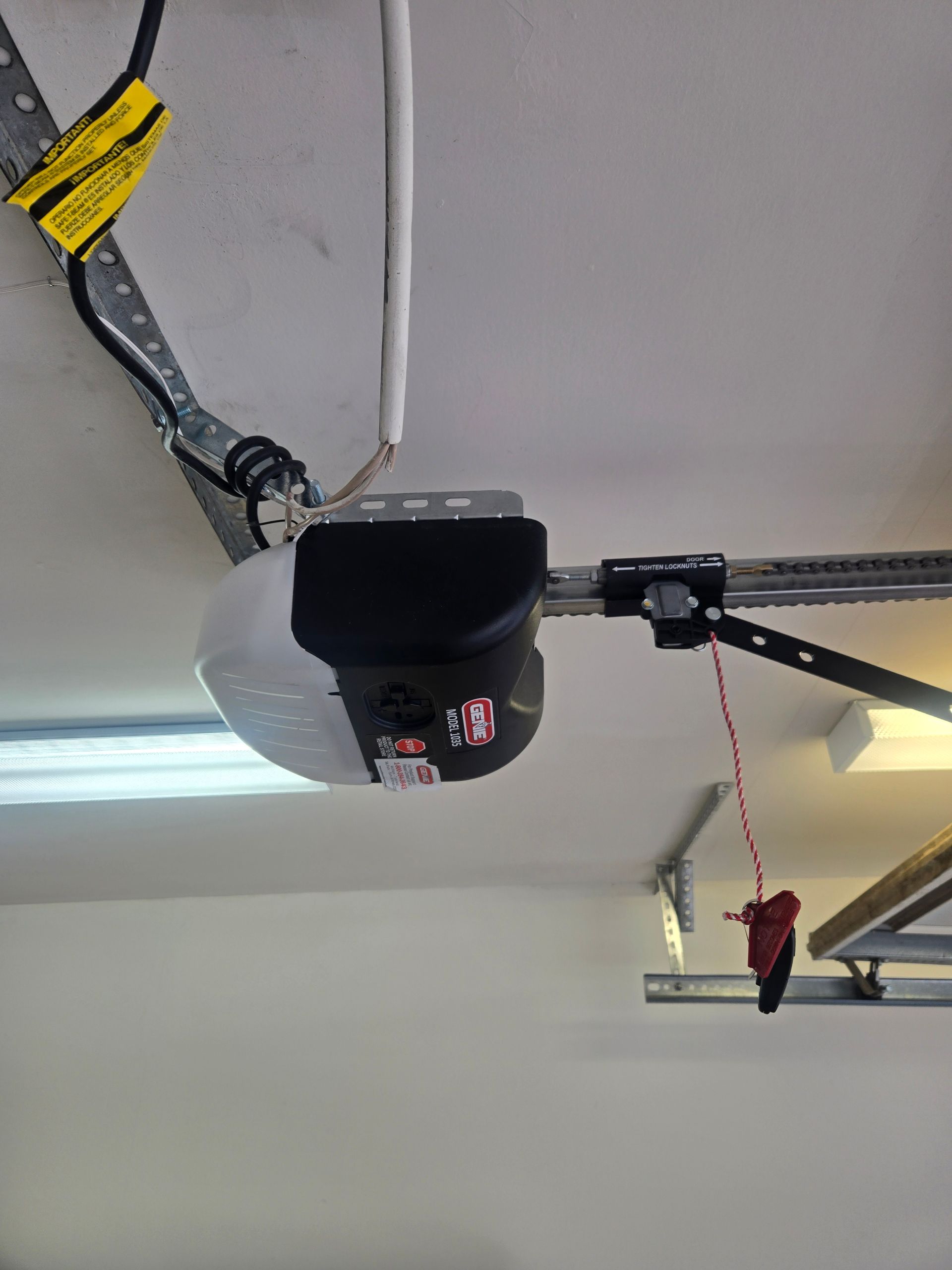 Garage door opener mounted on ceiling, with power cord and safety release.