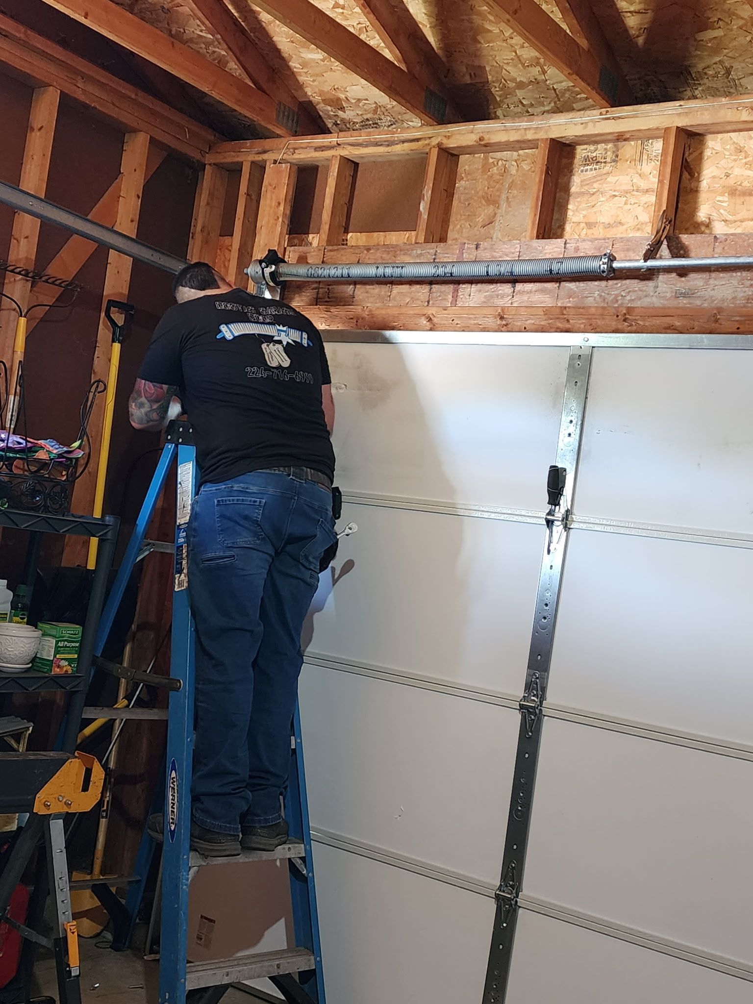 Person on a ladder, repairing a garage door.