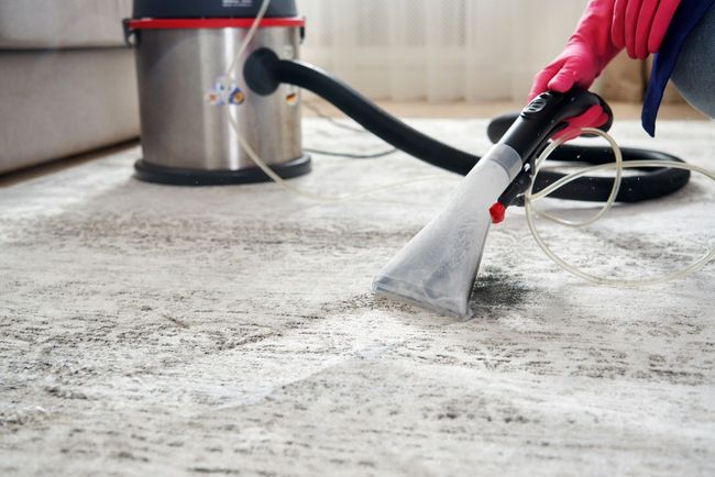 Person using a carpet cleaner on a light-colored rug in a home interior