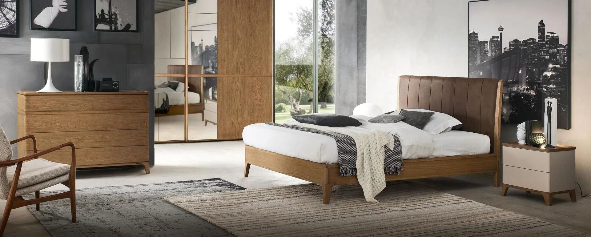 Camera da letto con mobili in legno: letto, cassettiera e comodino. Pareti grigie, quadri e tappeto.