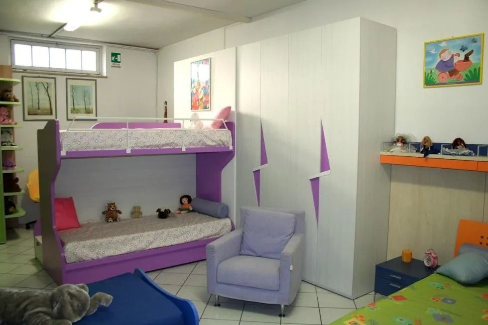 Cameretta per bambini con letto a castello, armadio, poltrona e decorazioni colorate. Combinazione di colori viola e bianco.