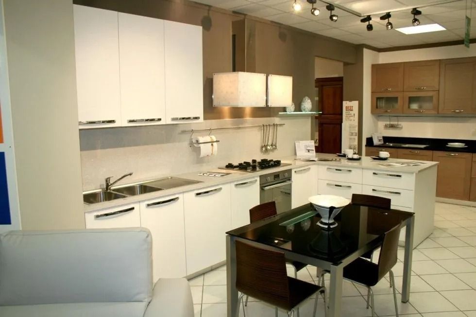 Cucina moderna con mobili bianchi, elettrodomestici in acciaio inossidabile e un piccolo tavolo da pranzo.