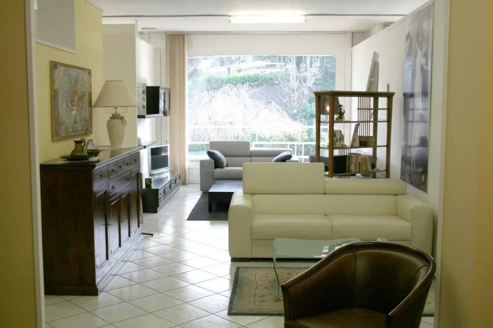 Ripresa interna di un soggiorno arredato con divani bianchi, un mobile in legno scuro e una vista sugli alberi attraverso una finestra.