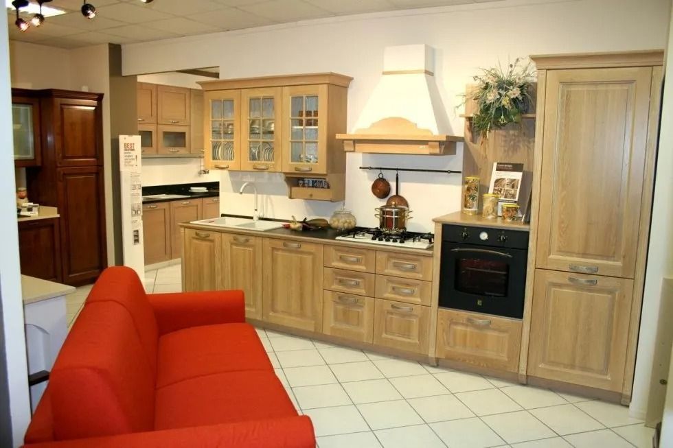 Cucina con mobili in legno chiaro, forno incorporato e divano rosso.