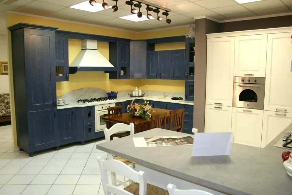 Espositore da cucina blu e bianco con mobili, fornelli e tavolo, che mostra l'allestimento della cucina.