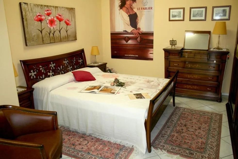 Camera da letto con mobili in legno: letto, comodini, cassettiera. Decorazioni floreali, tappeti e una poltrona in pelle.