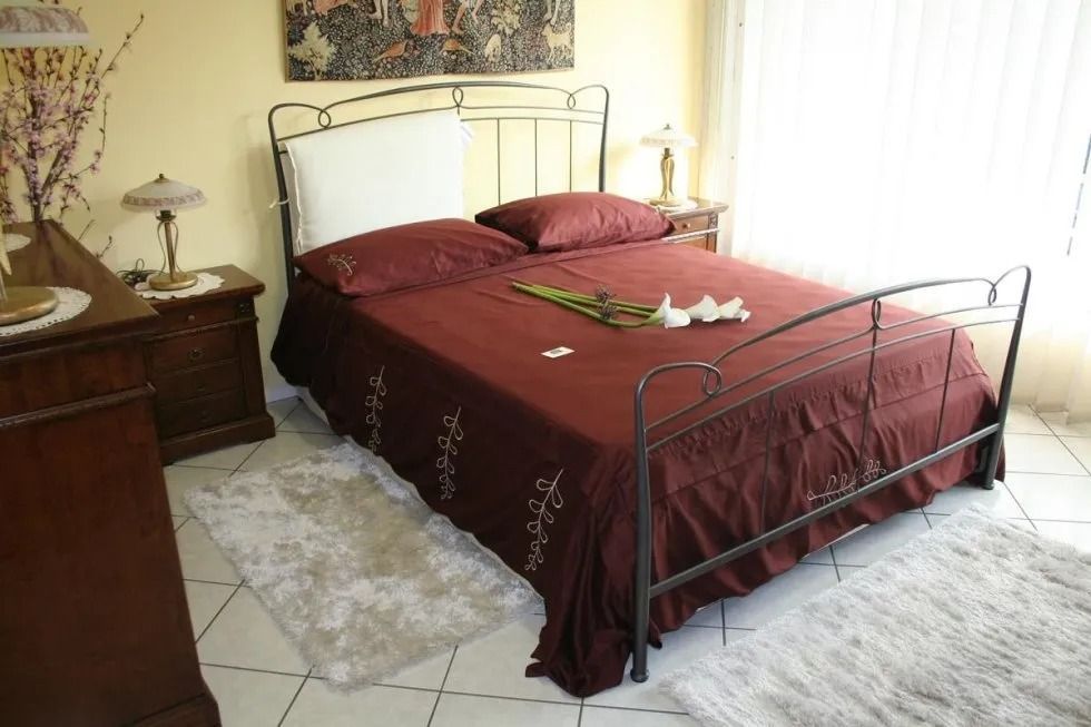 Camera da letto con copriletto bordeaux, struttura del letto in ferro, tappeto, comodini e quadri alle pareti.