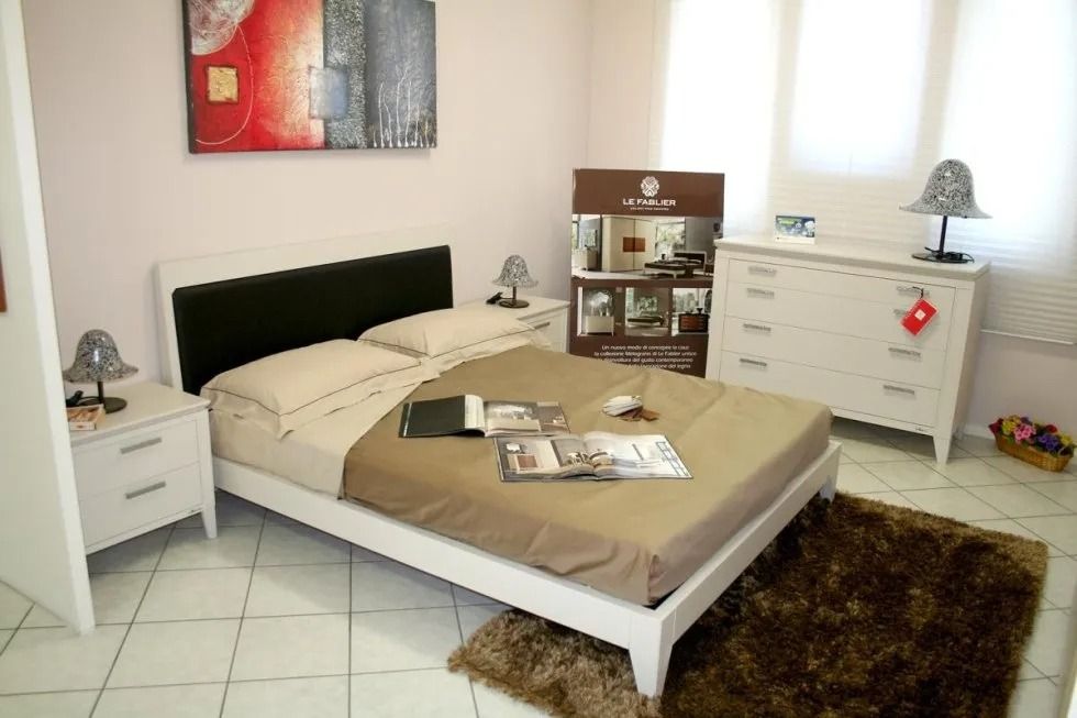 Camera da letto con letto bianco, comodini e cassettiera. Tappeto e biancheria da letto marroni. Opere d'arte alla parete.