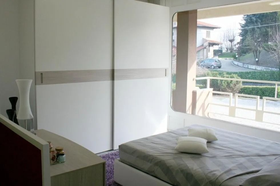 Camera da letto con armadio bianco con ante scorrevoli, letto e finestra con vista sulla strada.