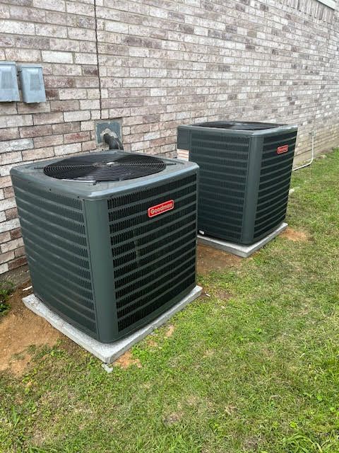 Two air conditioners are sitting next to each other in front of a brick wall.