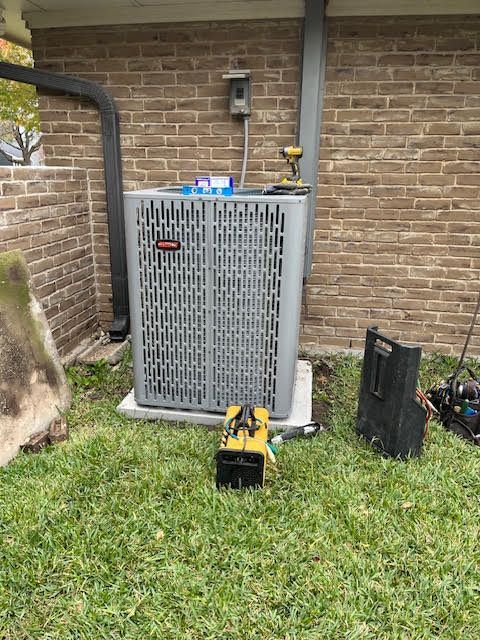 An air conditioner is sitting in the grass next to a brick wall.